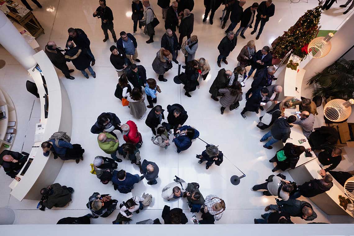 Imaxe dende arriba da entrada dunha empresa, na mesma hai dos mostradores e moitas persoas de diferentes 