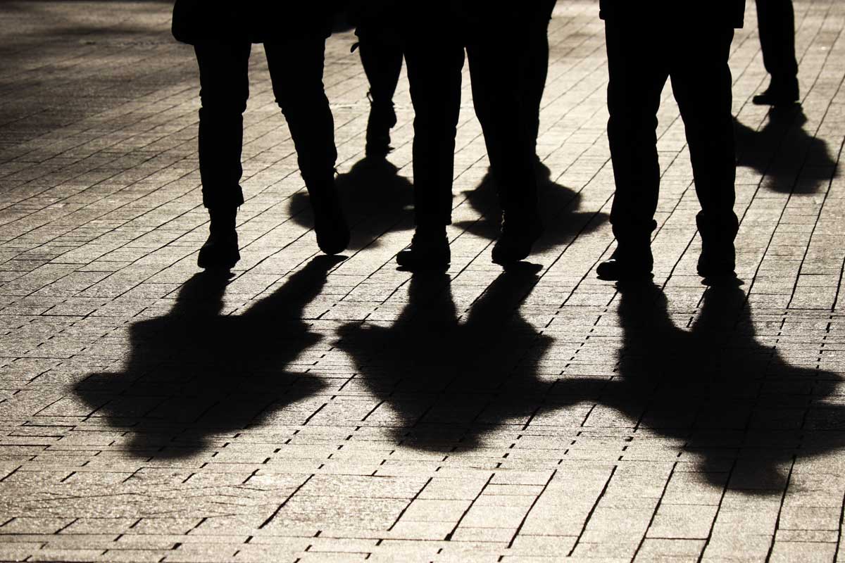 Siluetas e sombras de persoas camiñando pola rúa.