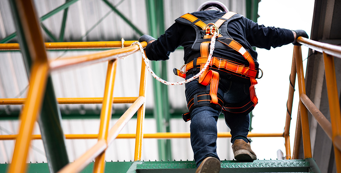 Unha persoa equipada con roupa de seguridade sobe por unha escaleira industrial.
